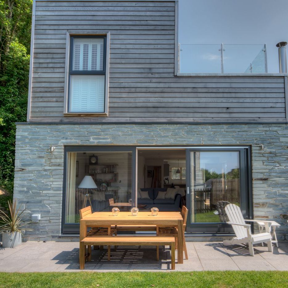 Modern house with wooden and stone exterior, patio furniture, and glass balcony