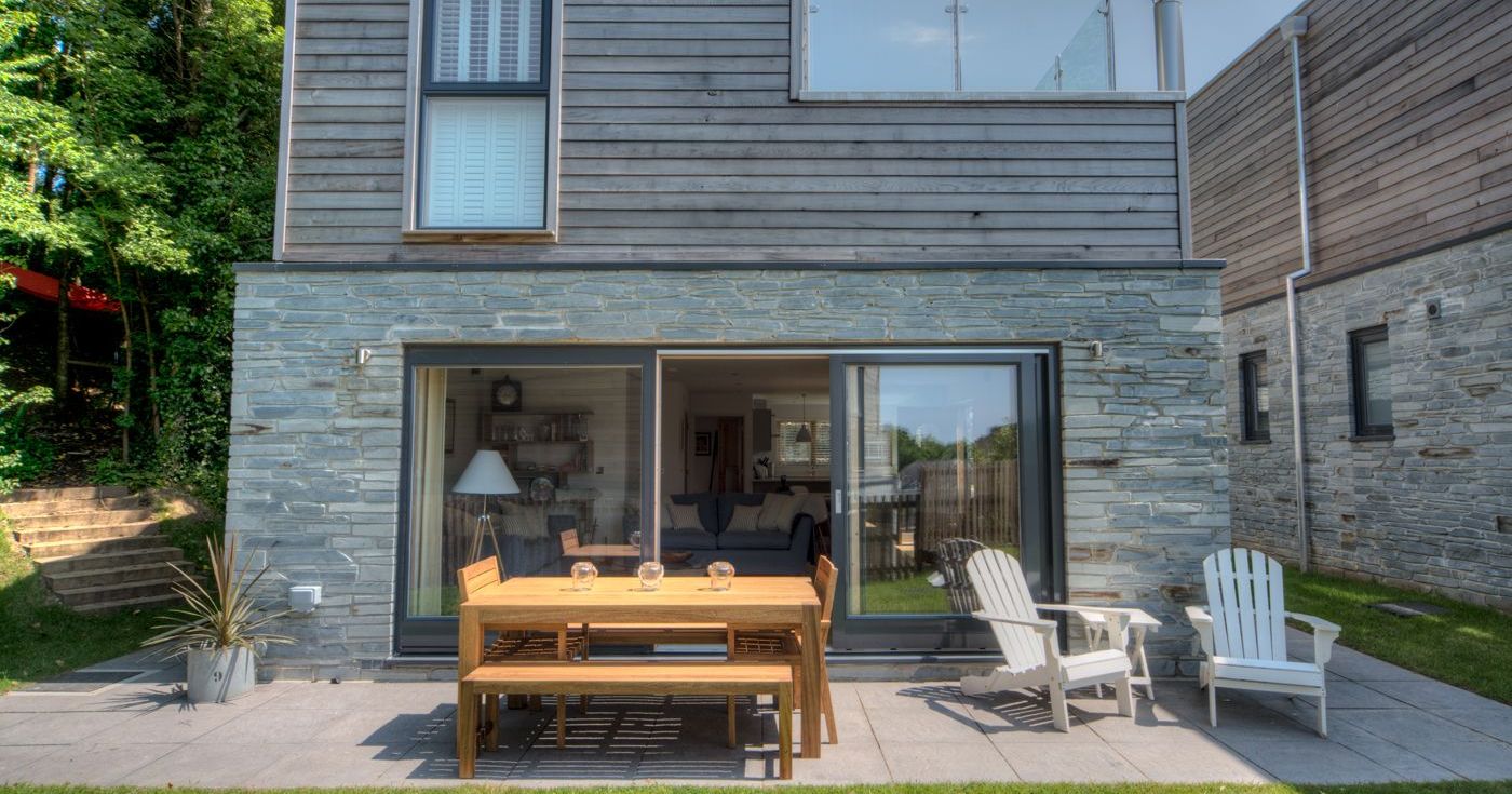 Modern house with wooden and stone exterior, patio furniture, and glass balcony