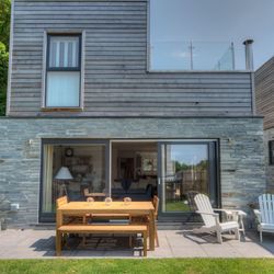 Modern house with wooden and stone exterior, patio furniture, and glass balcony