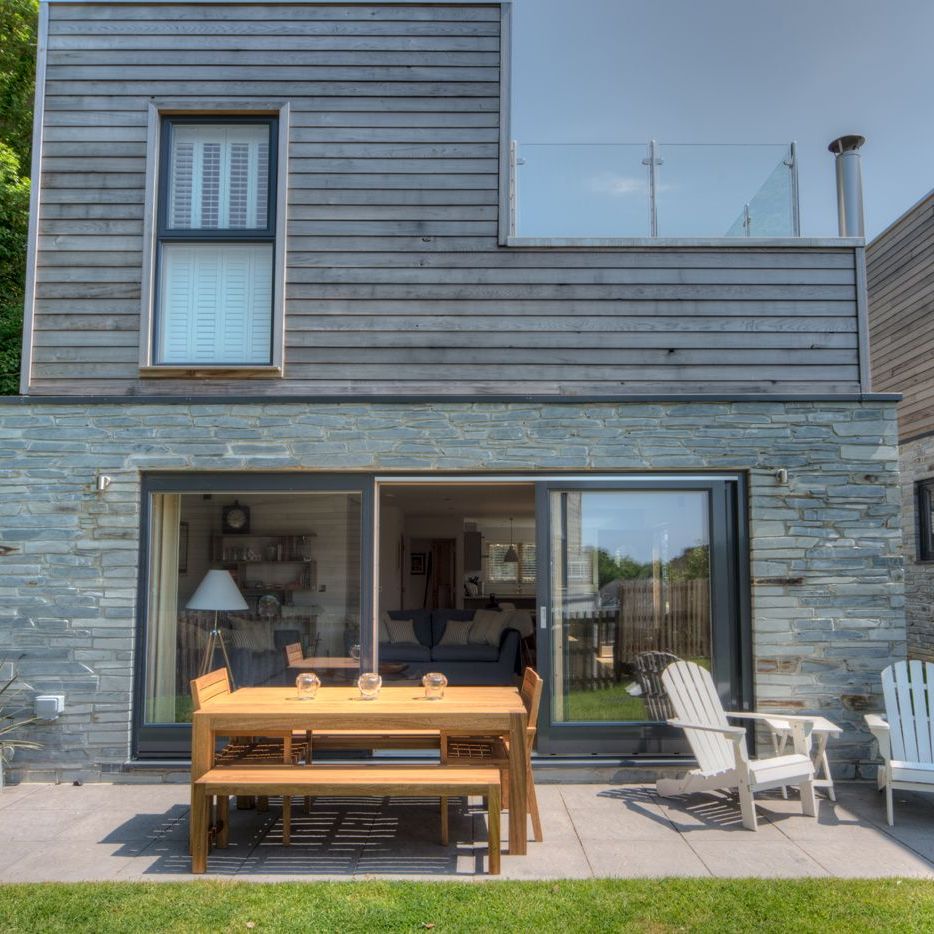 Modern house with wooden and stone exterior, patio furniture, and glass balcony