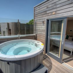 Private outdoor hot tub on a wooden deck with a view into a modern bedroom