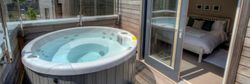 Private outdoor hot tub on a wooden deck with a view into a modern bedroom