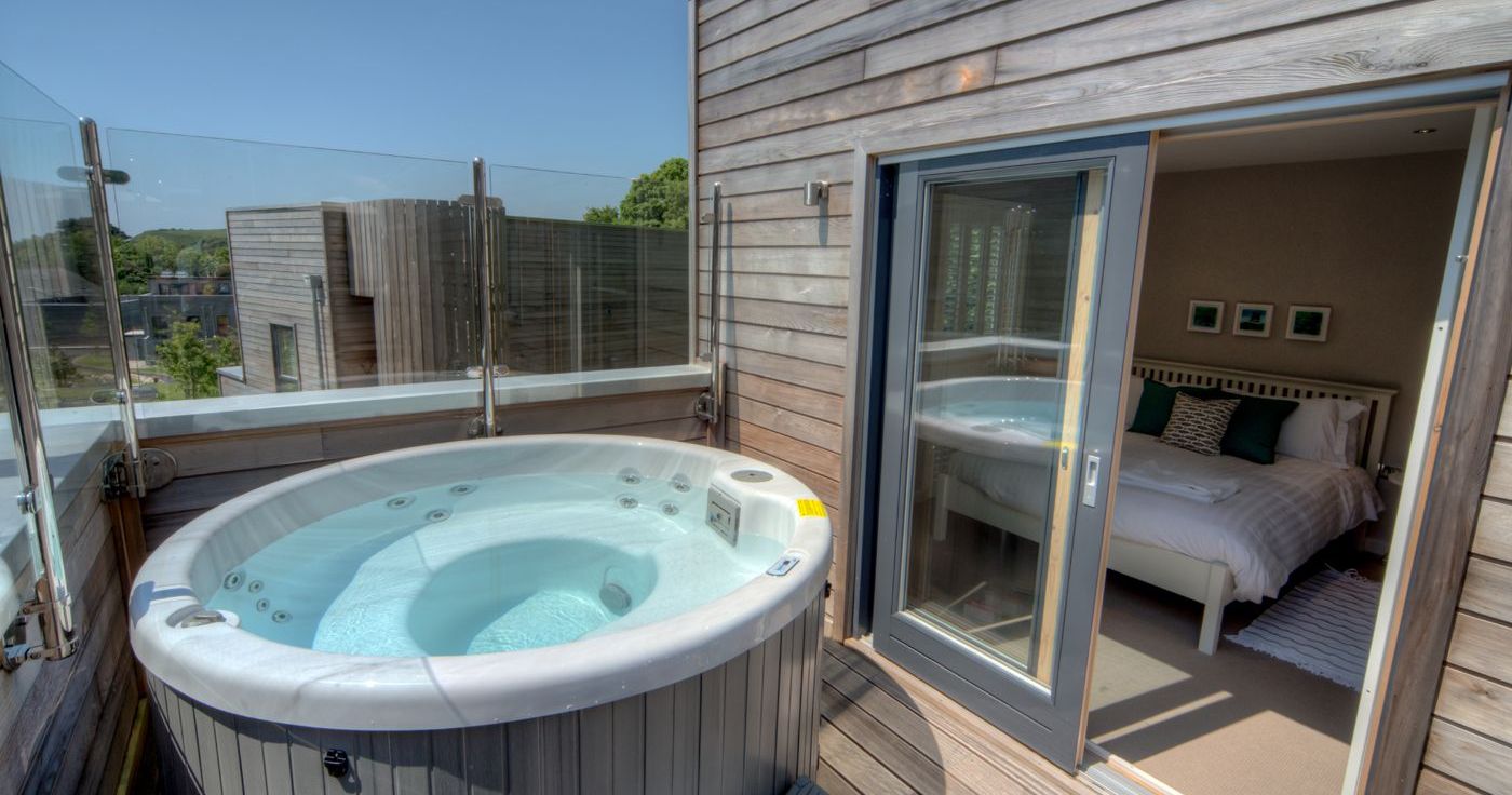 Private outdoor hot tub on a wooden deck with a view into a modern bedroom