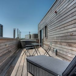 Modern wooden rooftop patio with lounge chair and table set under a clear sky