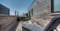 Modern wooden rooftop patio with lounge chair and table set under a clear sky