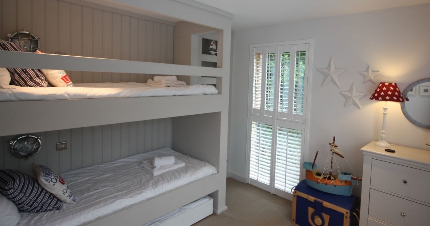 Children's bedroom with bunk beds, nautical decor, and white shutters on the window