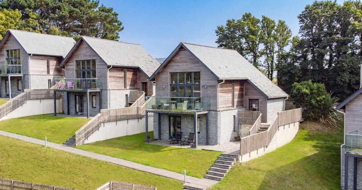 Modern wooden and stone houses with balconies set on sloped green lawns.