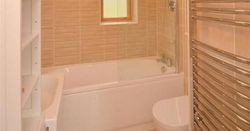 Modern bathroom with beige tiles, bathtub, shower, towel radiator, and small window.