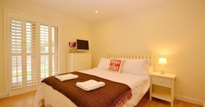 Cozy bedroom with double bed, bedside table, chest of drawers, TV and French doors.