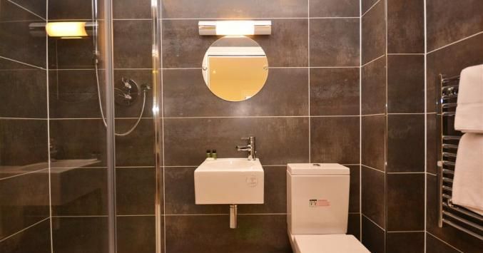 Modern bathroom with dark tiles, a small sink, toilet, and glass shower enclosure.