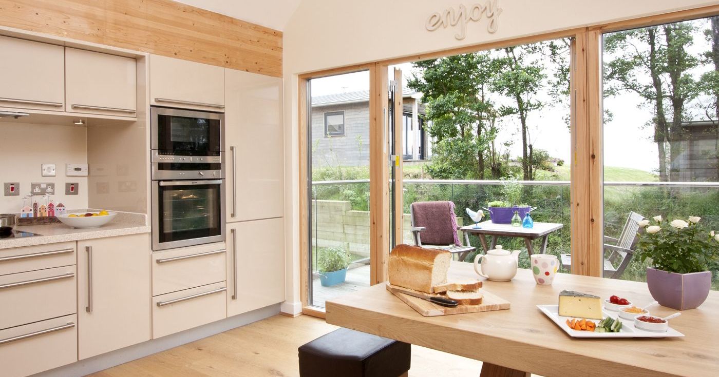 Modern kitchen with wooden accents and large glass doors overlooking a patio with outdoor seating.