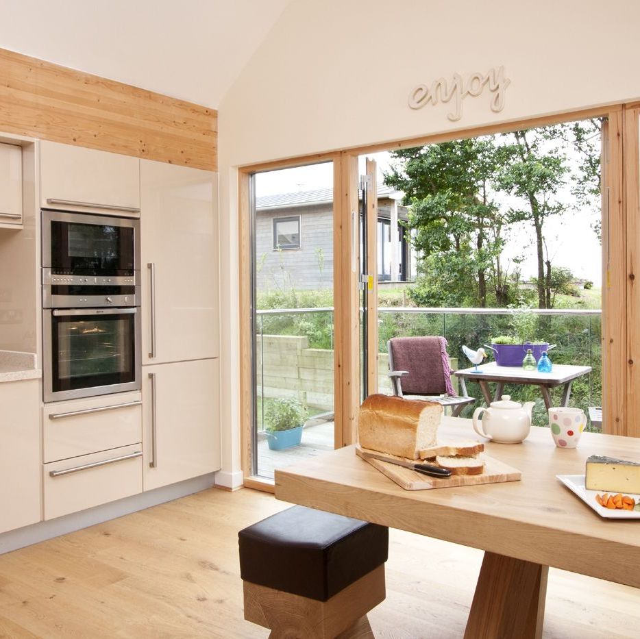 Modern kitchen with wooden accents and large glass doors overlooking a patio with outdoor seating.