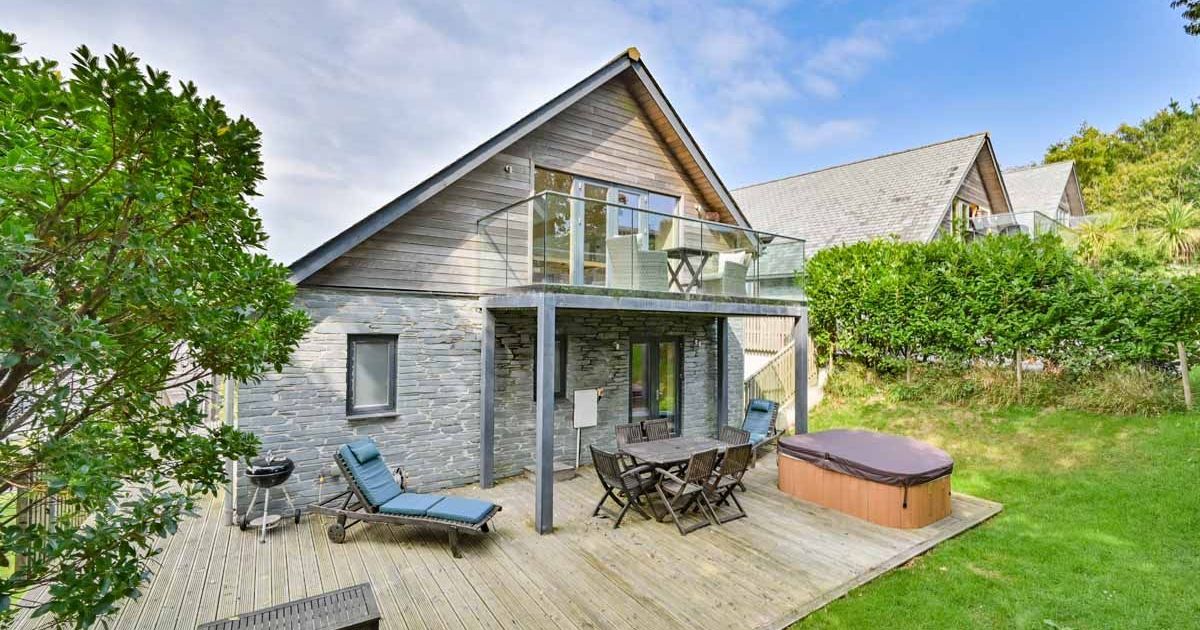 Modern house with large wooden deck, outdoor seating, hot tub, and balcony