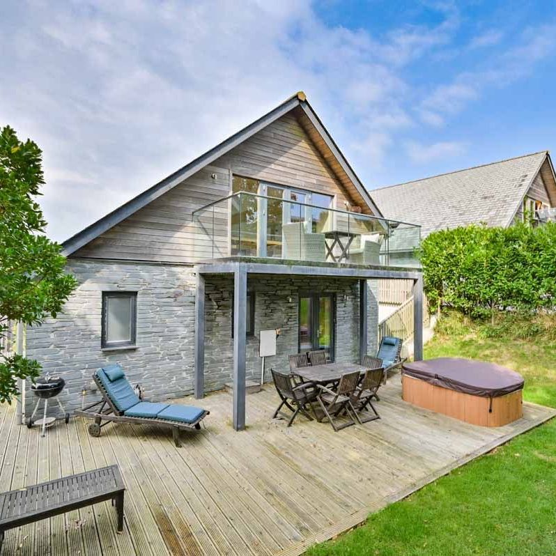 Modern house with large wooden deck, outdoor seating, hot tub, and balcony