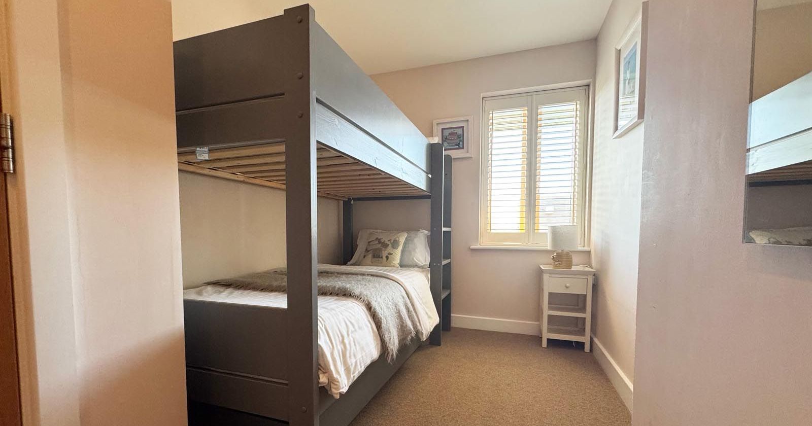 A small bedroom with a dark gray bunk bed, a window with white shutters, and a small white nightstand.