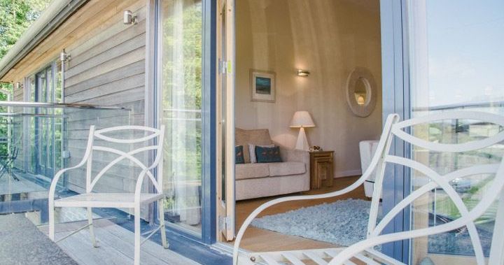 Outdoor seating area on a balcony with a view into a cozy living room through glass doors.