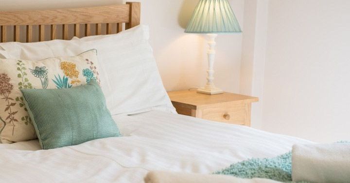 Cozy, well-lit bedroom with a wooden bed, floral cushion, green pillow, bedside table, and lamp.