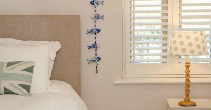 Cozy bedroom with a bed, decorative pillow, fish wall hanging, window with blinds, and a nightstand with a lamp.