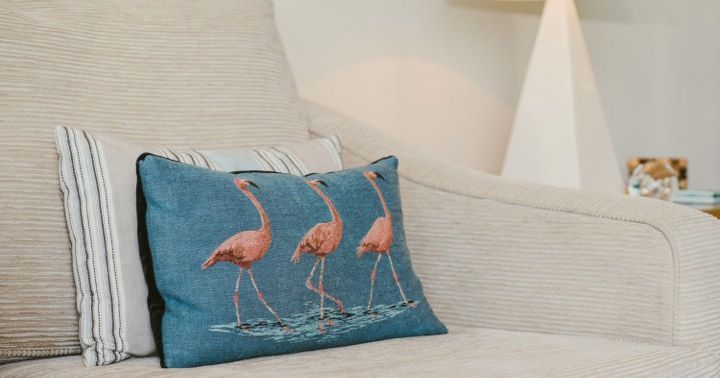 Couch with pillows, including one with pink flamingos, and a lamp in the background