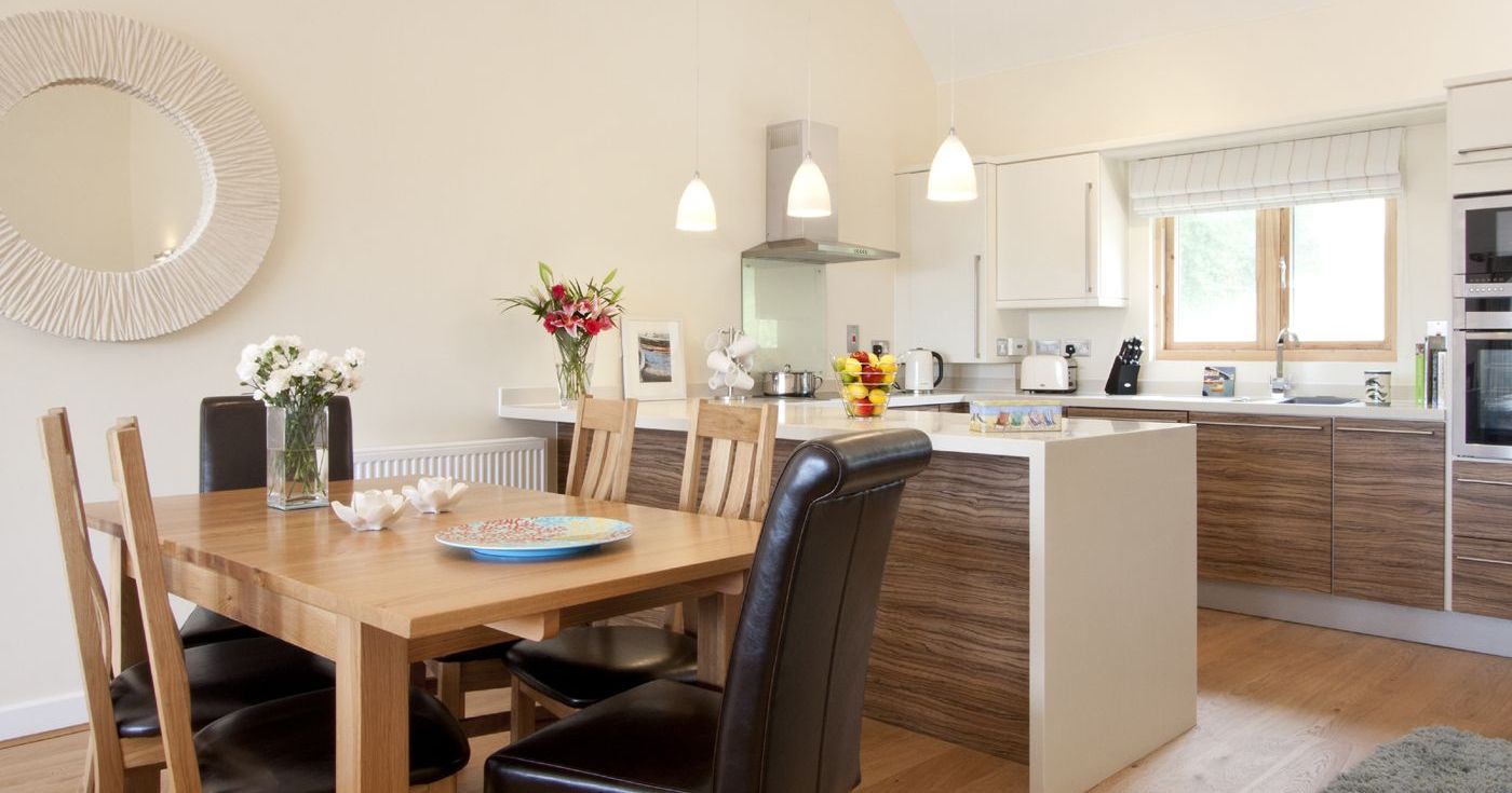Modern kitchen and dining area with wooden table and chairs, pendant lighting, and decorative flowers.