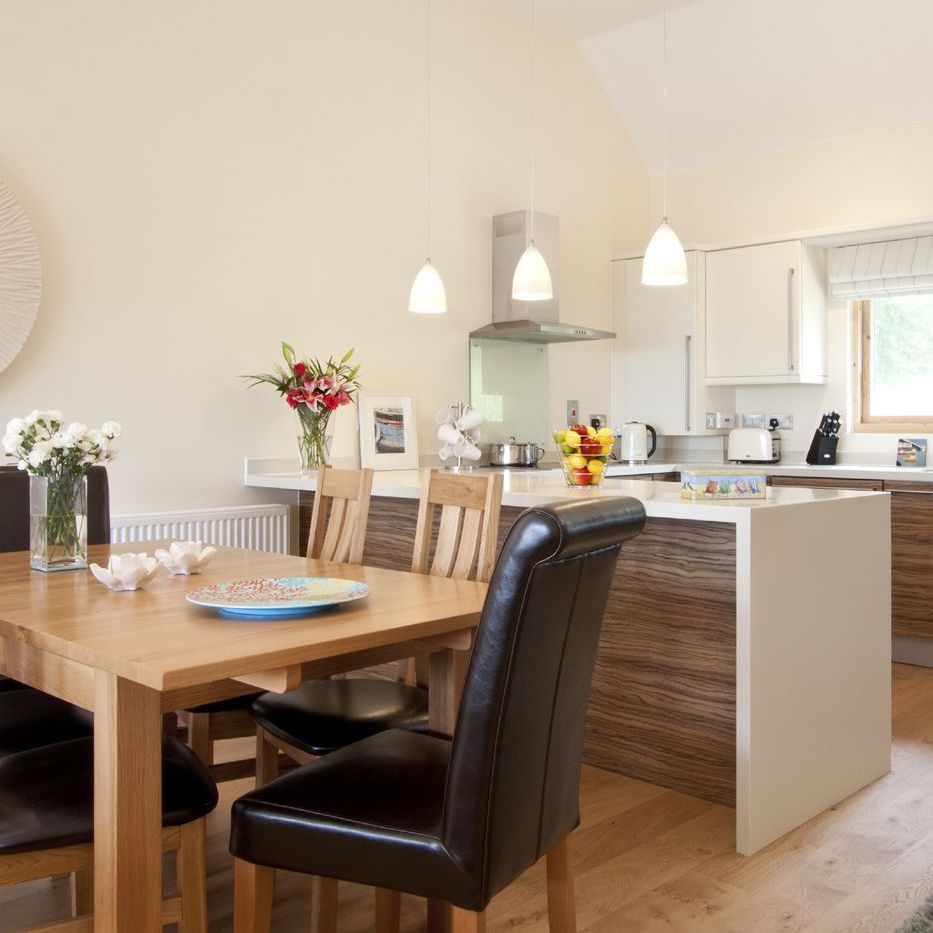 Modern kitchen and dining area with wooden table and chairs, pendant lighting, and decorative flowers.