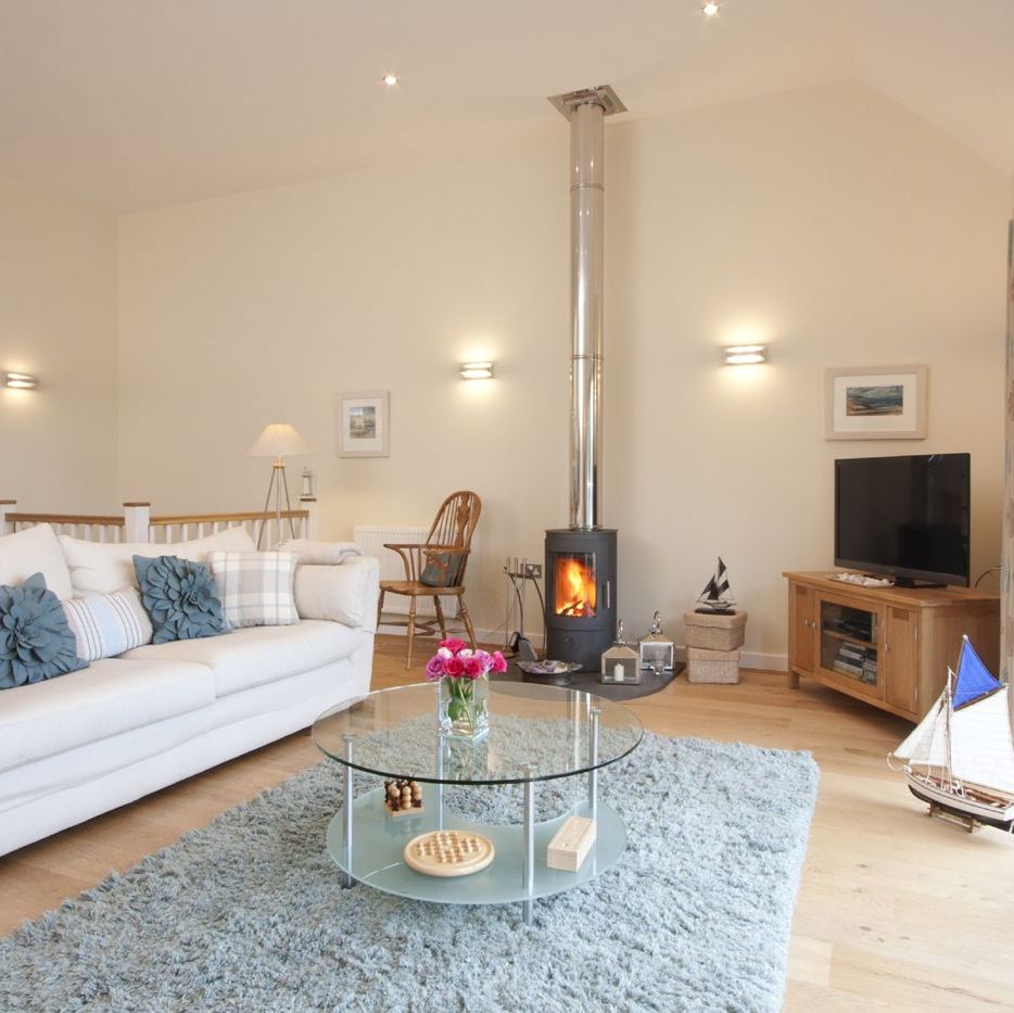Modern living room with light decor, wood stove, and glass coffee table