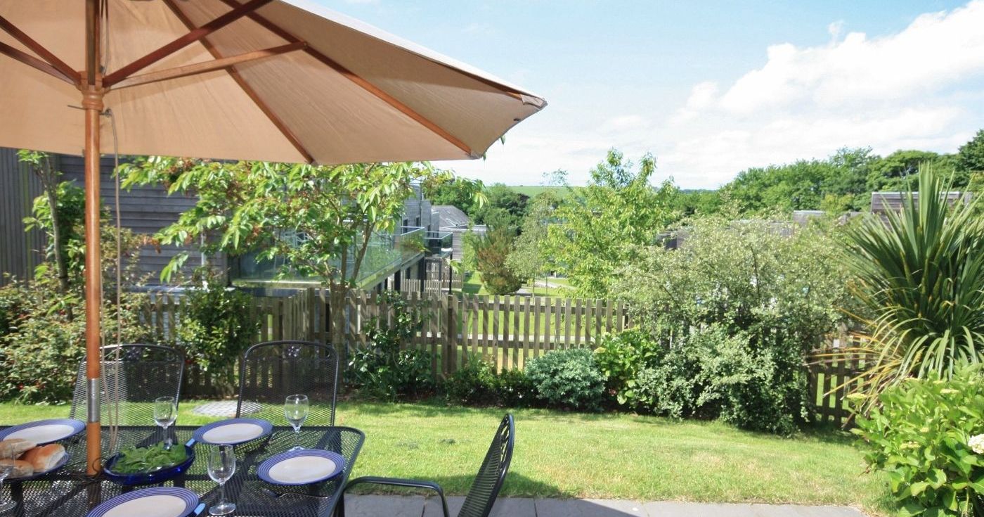 Outdoor patio dining set with an umbrella, overlooking a garden and fenced yard