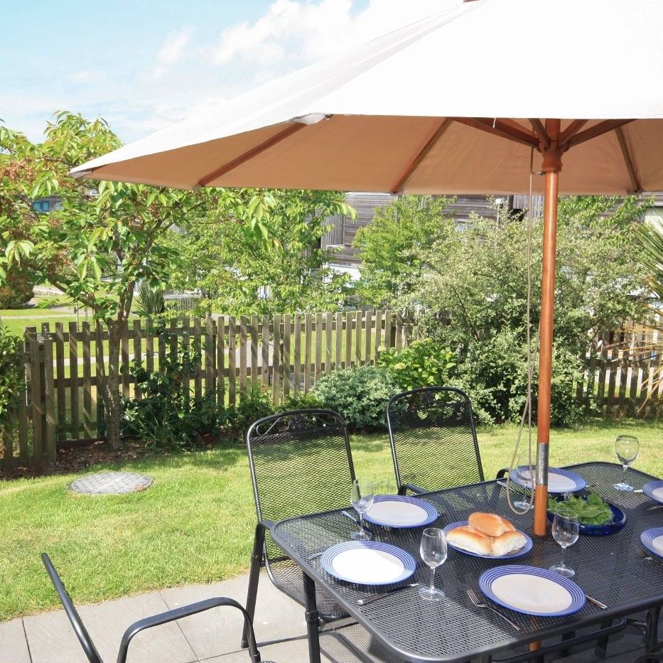 Outdoor patio dining area with black table and chairs under a large umbrella, set with plates and glasses in a green garden.