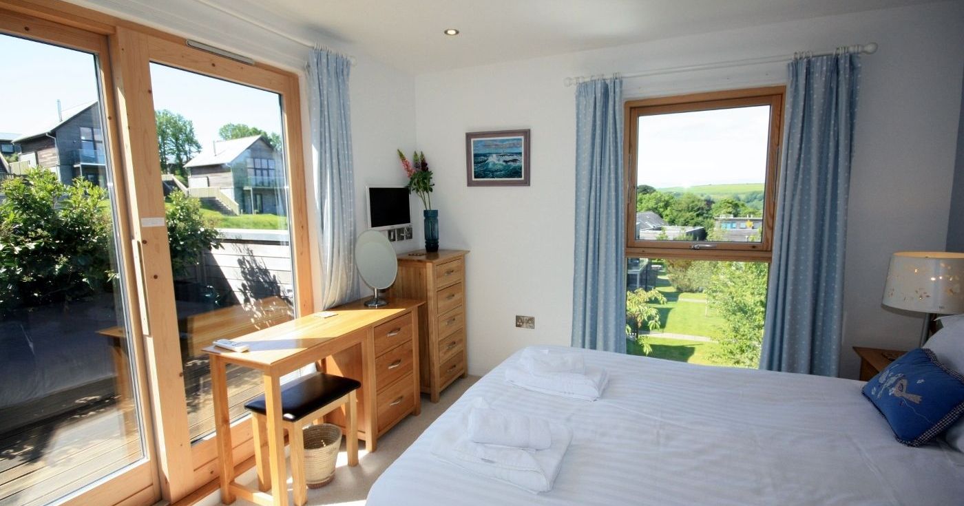 Bright bedroom with large windows and blue curtains overlooking a garden.