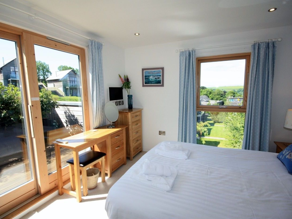 Bright bedroom with large windows and blue curtains overlooking a garden.