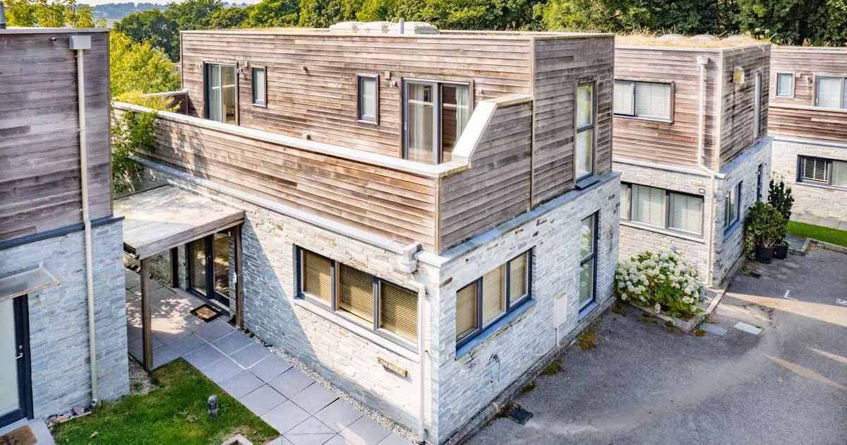 Modern house with stone and wood exterior, featuring large windows and an outdoor terrace.