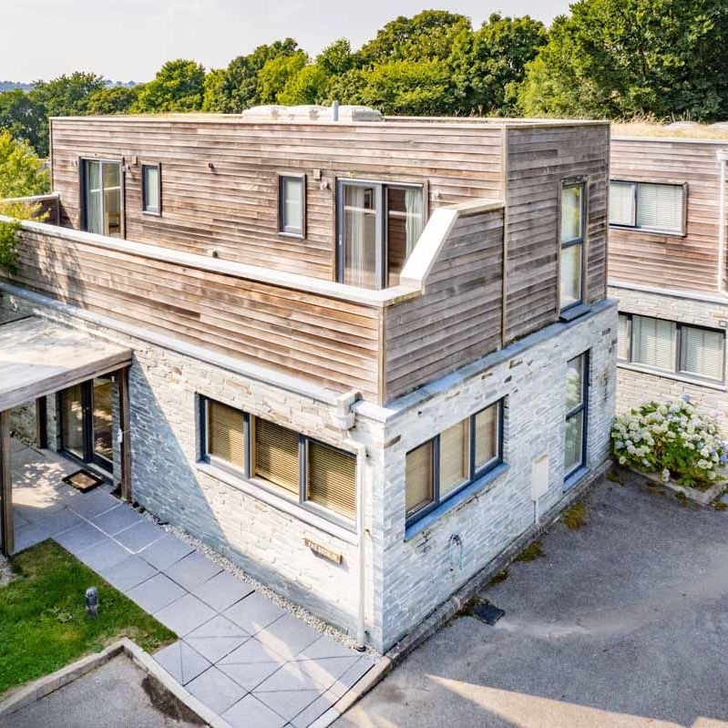 Modern house with stone and wood exterior, featuring large windows and an outdoor terrace.