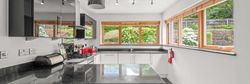 Modern kitchen with black countertops, white cabinets, and large windows overlooking a garden.