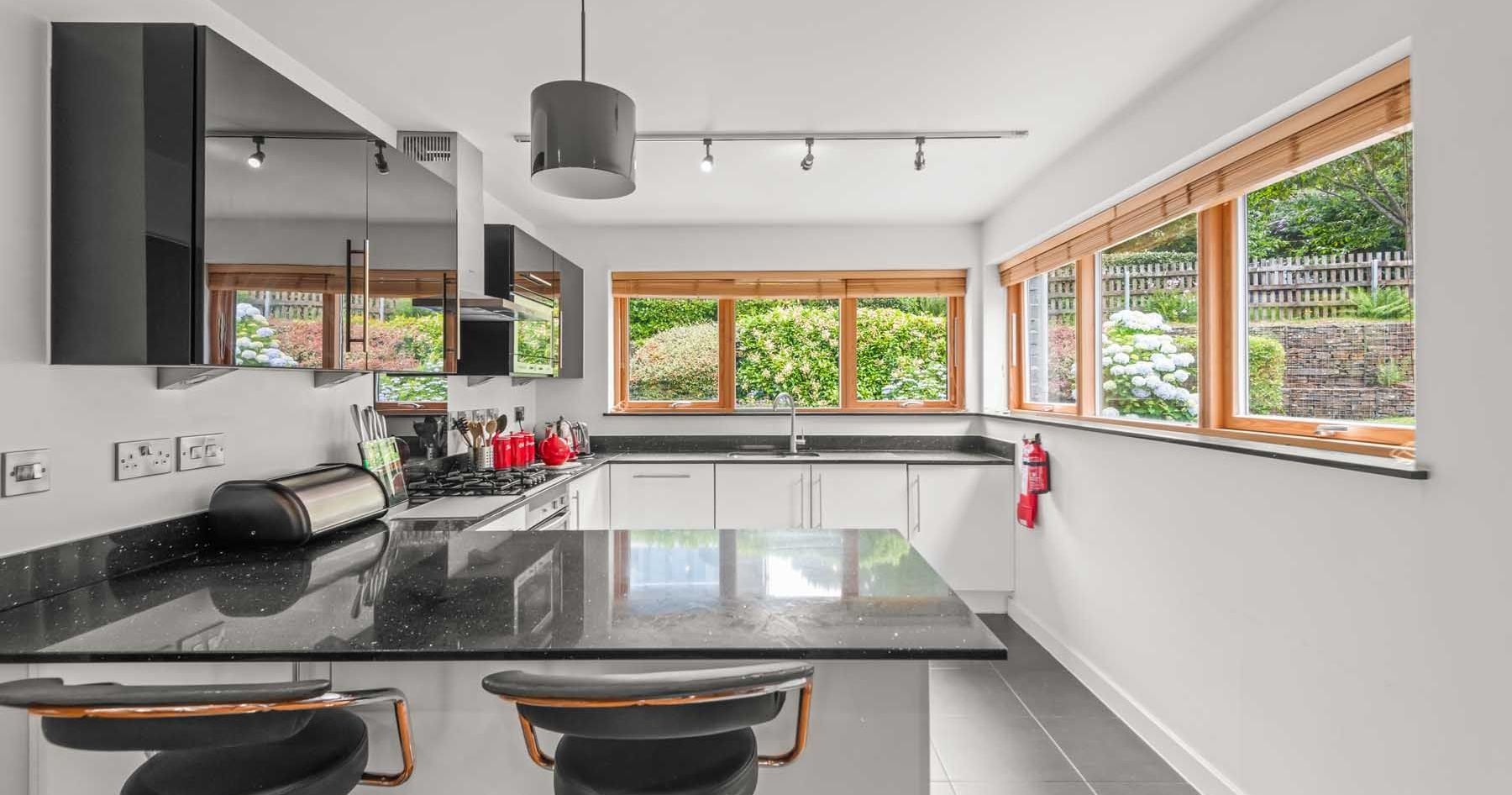 Modern kitchen with black countertops, white cabinets, and large windows overlooking a garden.