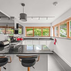 Modern kitchen with black countertops, white cabinets, and large windows overlooking a garden.