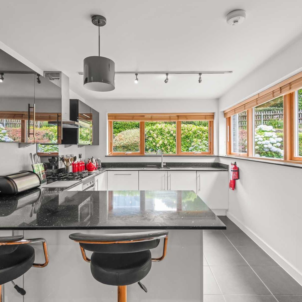 Modern kitchen with black countertops, white cabinets, and large windows overlooking a garden.