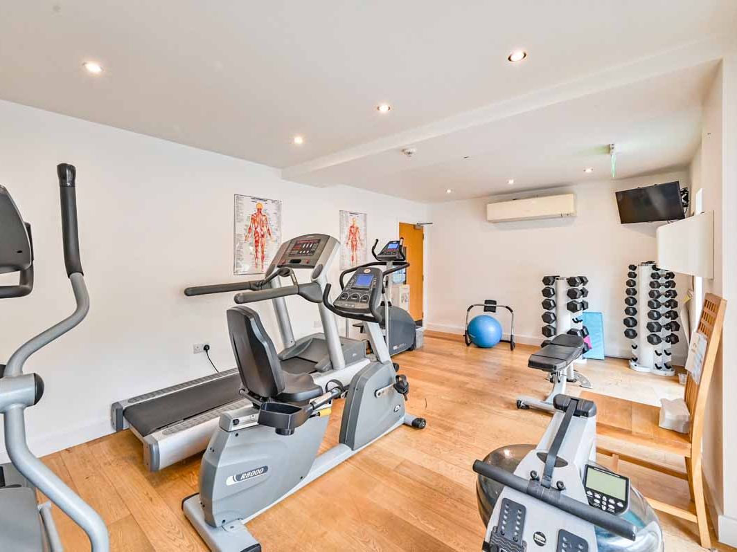 Small gym room with exercise equipment including treadmill, stationary bikes, dumbbells, and a blue exercise ball.