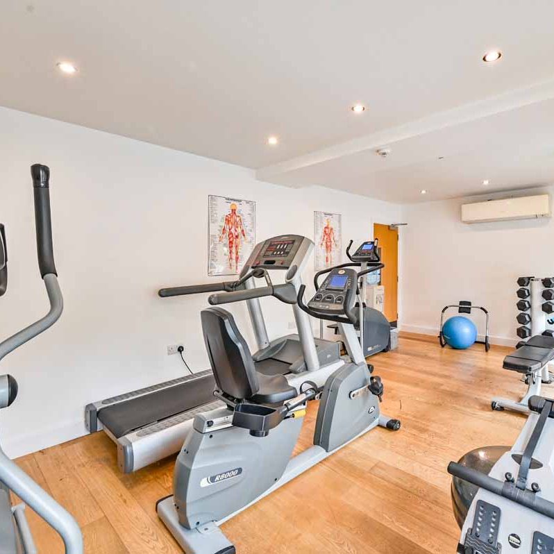 Small gym room with exercise equipment including treadmill, stationary bikes, dumbbells, and a blue exercise ball.