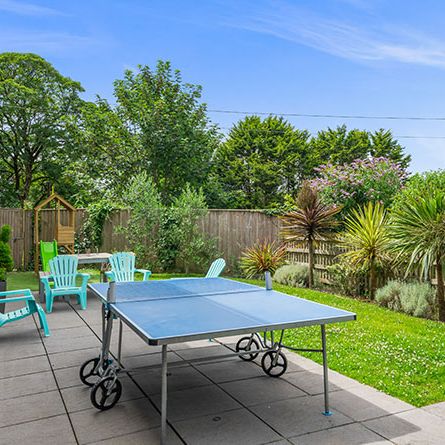 Outdoor patio area with table tennis table, garden chairs, and lush landscaping.