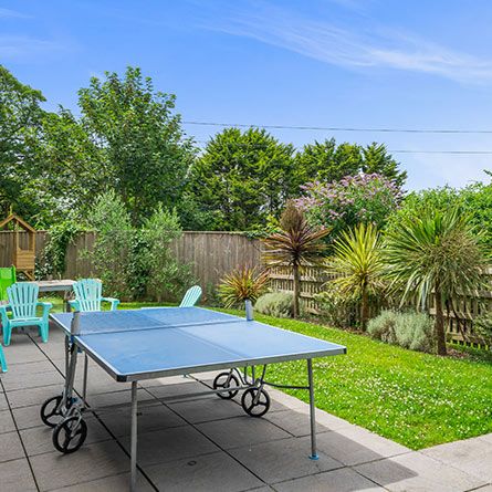 Outdoor patio area with table tennis table, garden chairs, and lush landscaping.