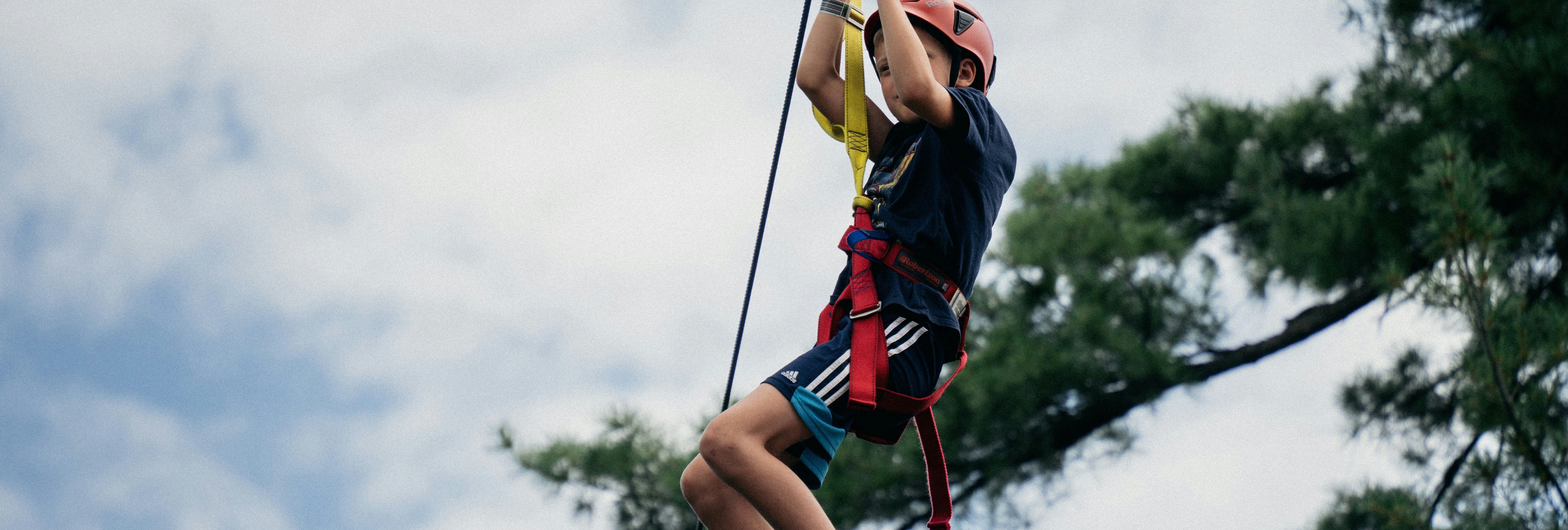 Child wearing a helmet and harness ziplining outdoors