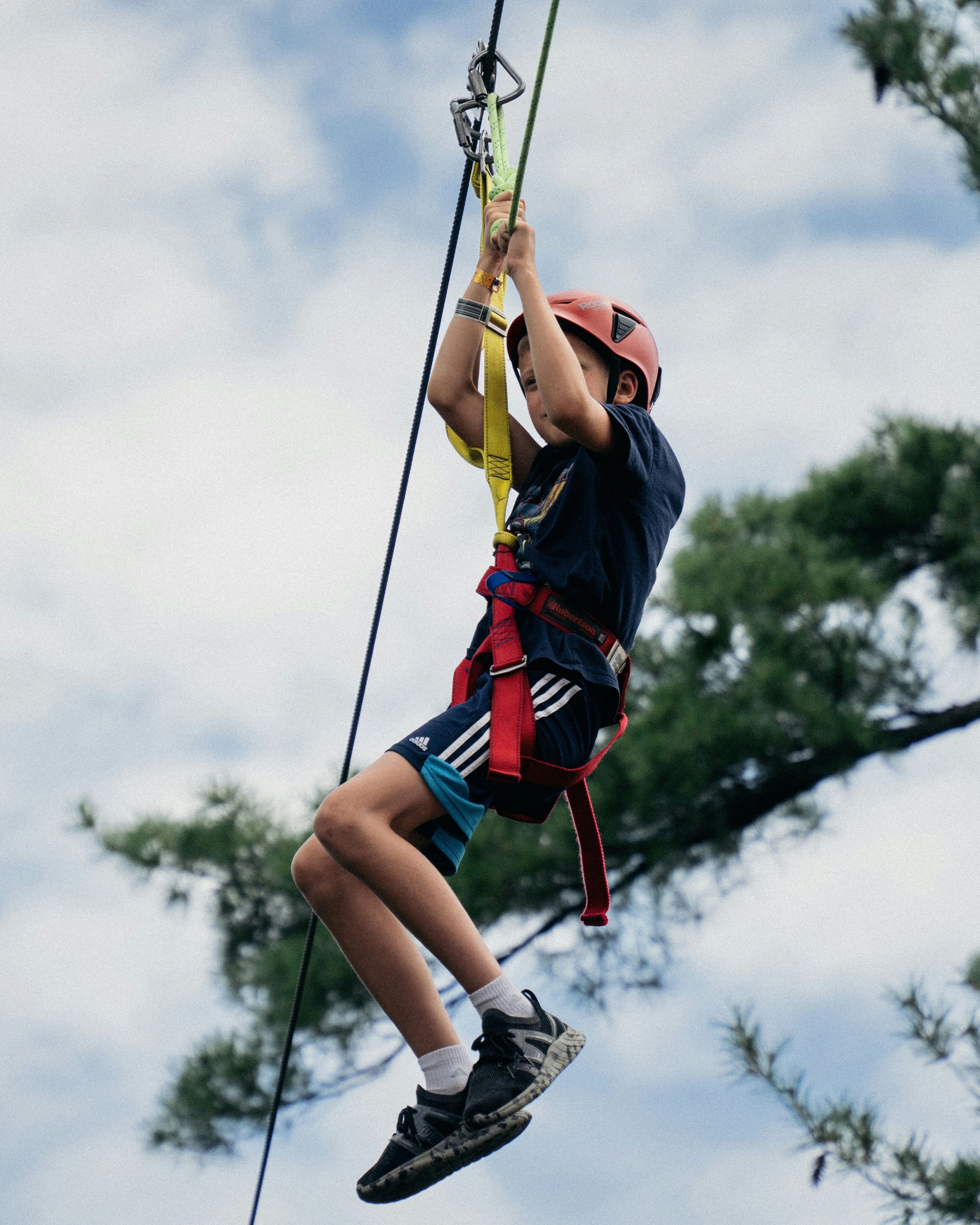 Child wearing a helmet and harness ziplining outdoors