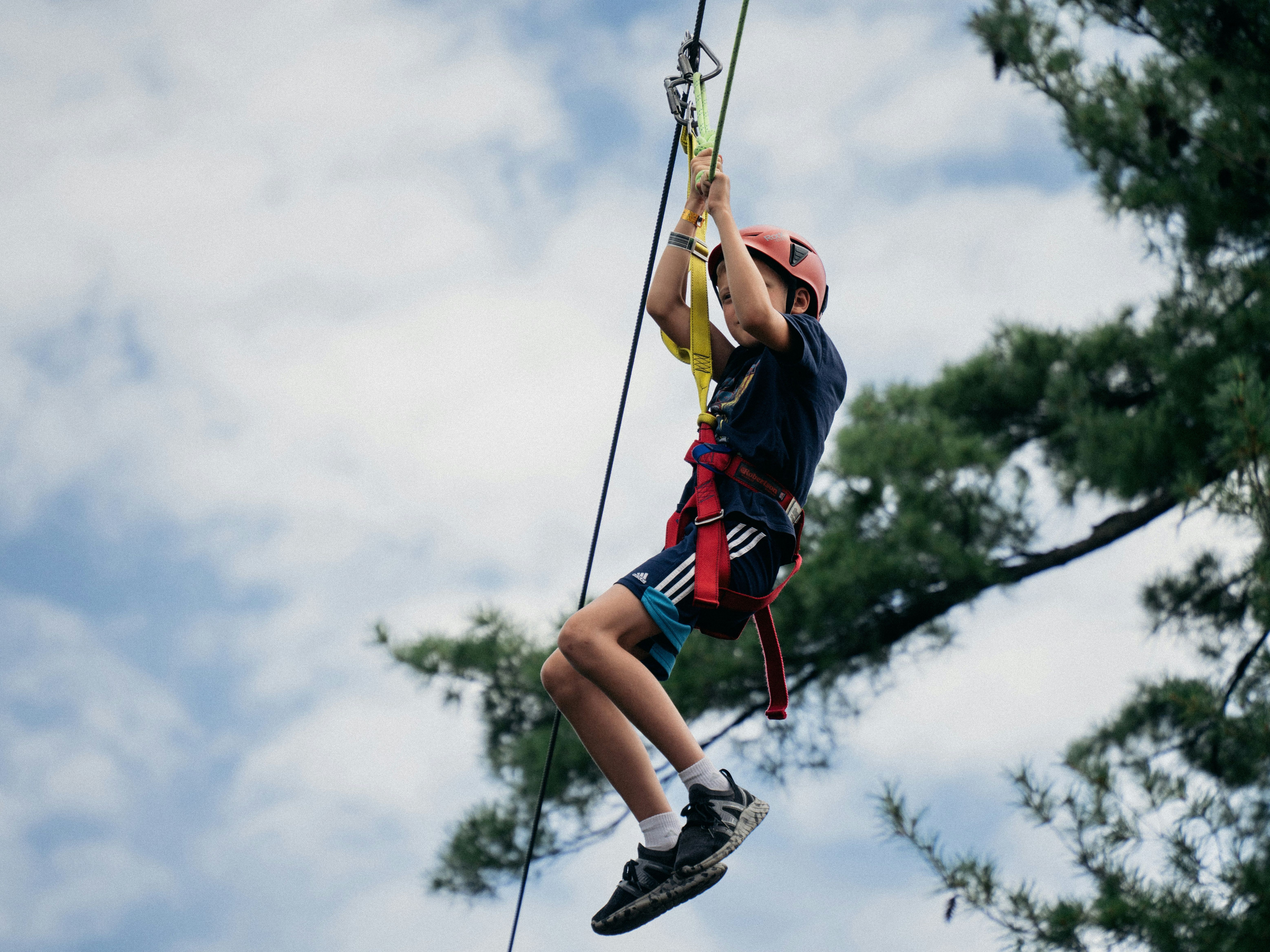 Child wearing a helmet and harness ziplining outdoors