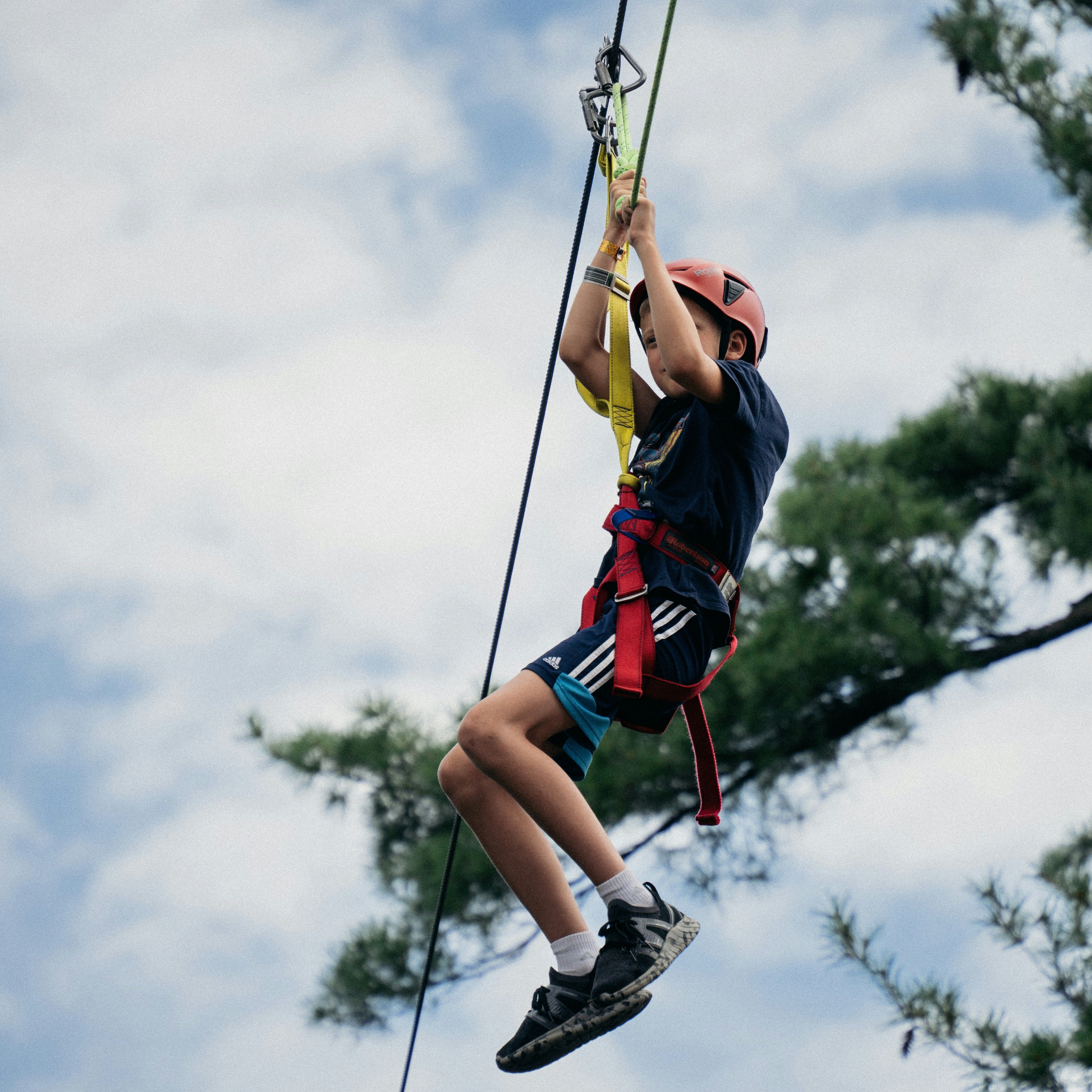 Child wearing a helmet and harness ziplining outdoors