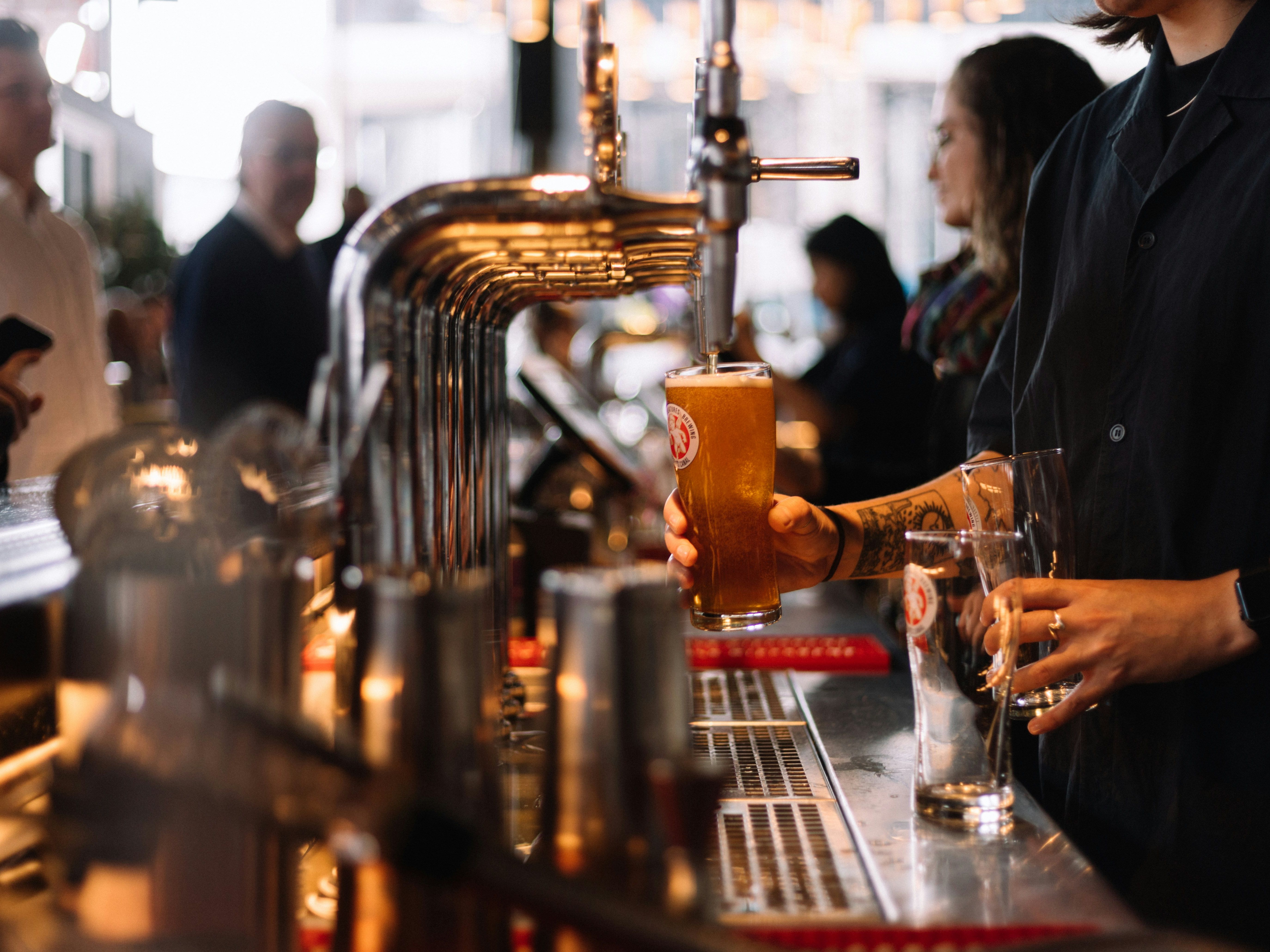 Bartender pouring a glass of beer from a tap at a busy bar