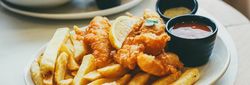 Plate of fish and chips with dipping sauces and a lemon wedge