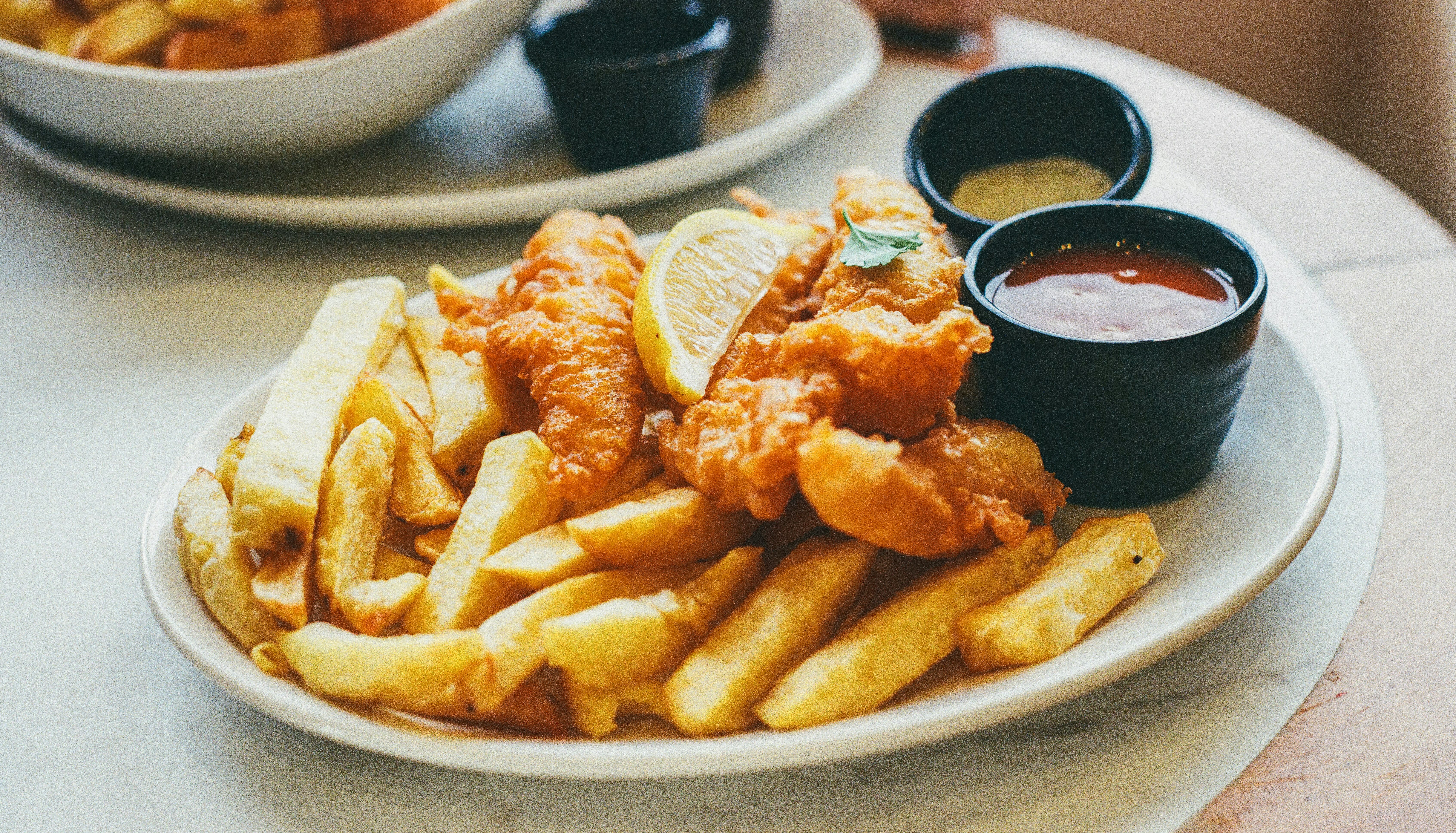Plate of fish and chips with dipping sauces and a lemon wedge