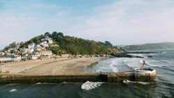 Coastal village with houses on a hill overlooking a sandy beach and a pier extending into the sea.