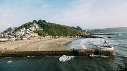 Coastal village with houses on a hill overlooking a sandy beach and a pier extending into the sea.