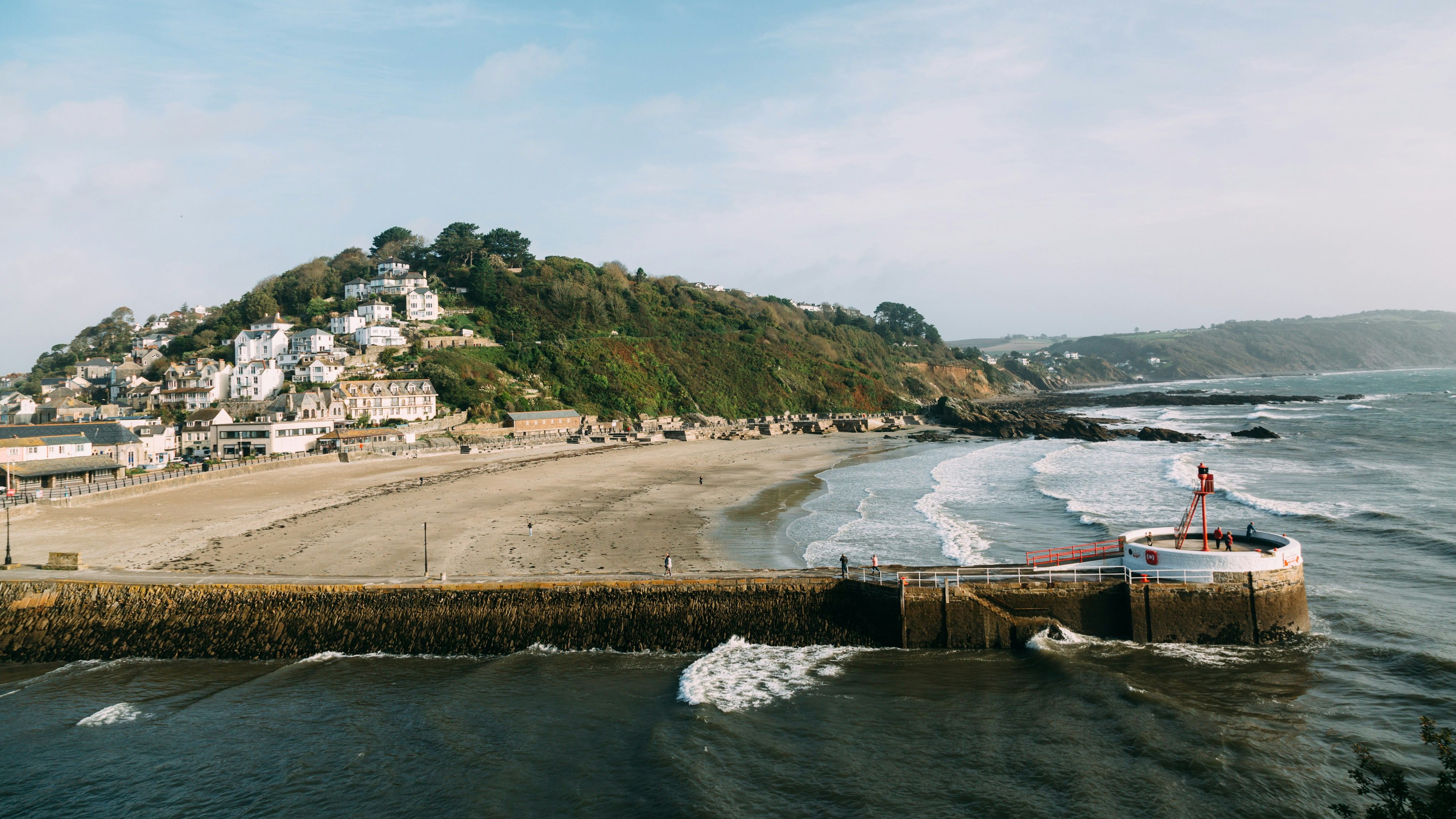 Coastal village with houses on a hill overlooking a sandy beach and a pier extending into the sea.